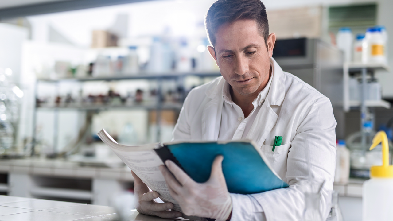 man in lab coat looking at a manual
